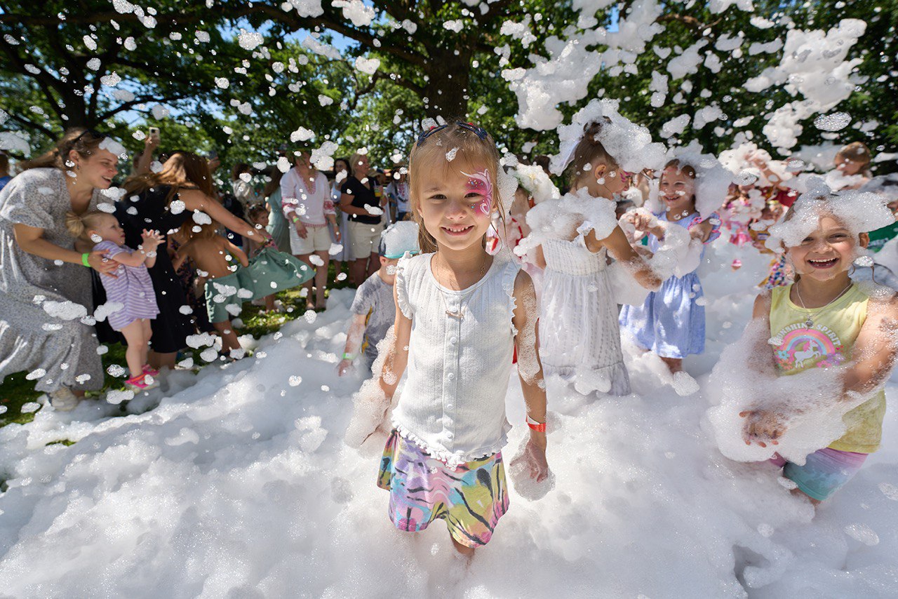 Children smiling and playing in foam bubbles at an outdoor event