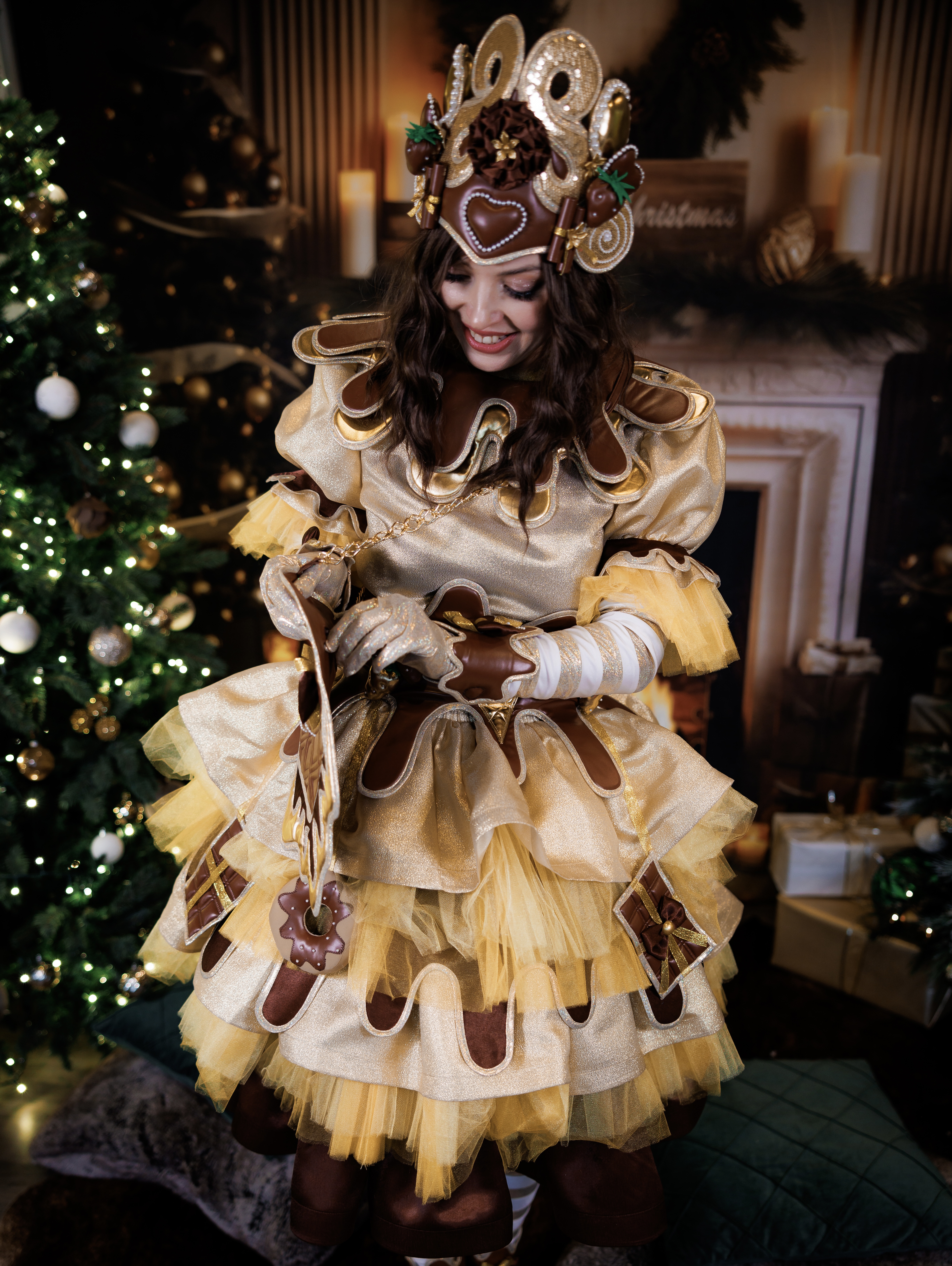 Chocolate fairy performer looking down while standing by a decorated Christmas tree