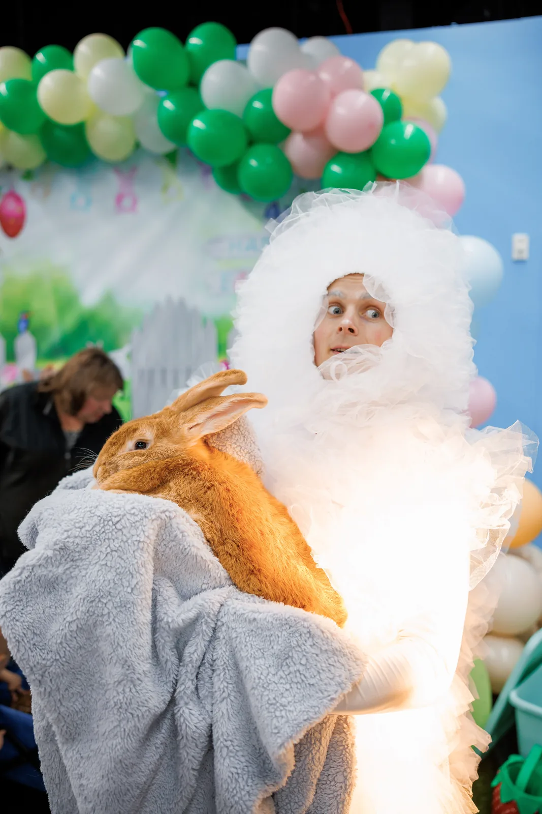 Entertainer in a fluffy white costume holding a large rabbit at an Easter event